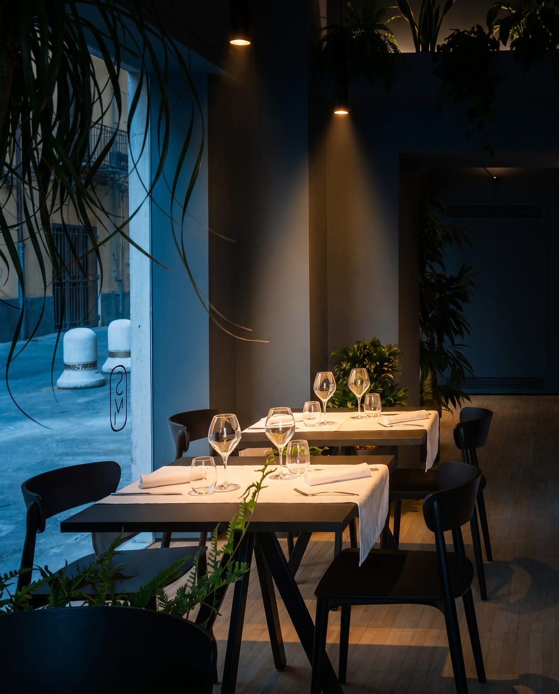La sala di Sobremesa a cena: tavoli apparecchiati con tovaglioli di lino sotto i faretti, il bancone di marmo e la piazza oltre la vetrata